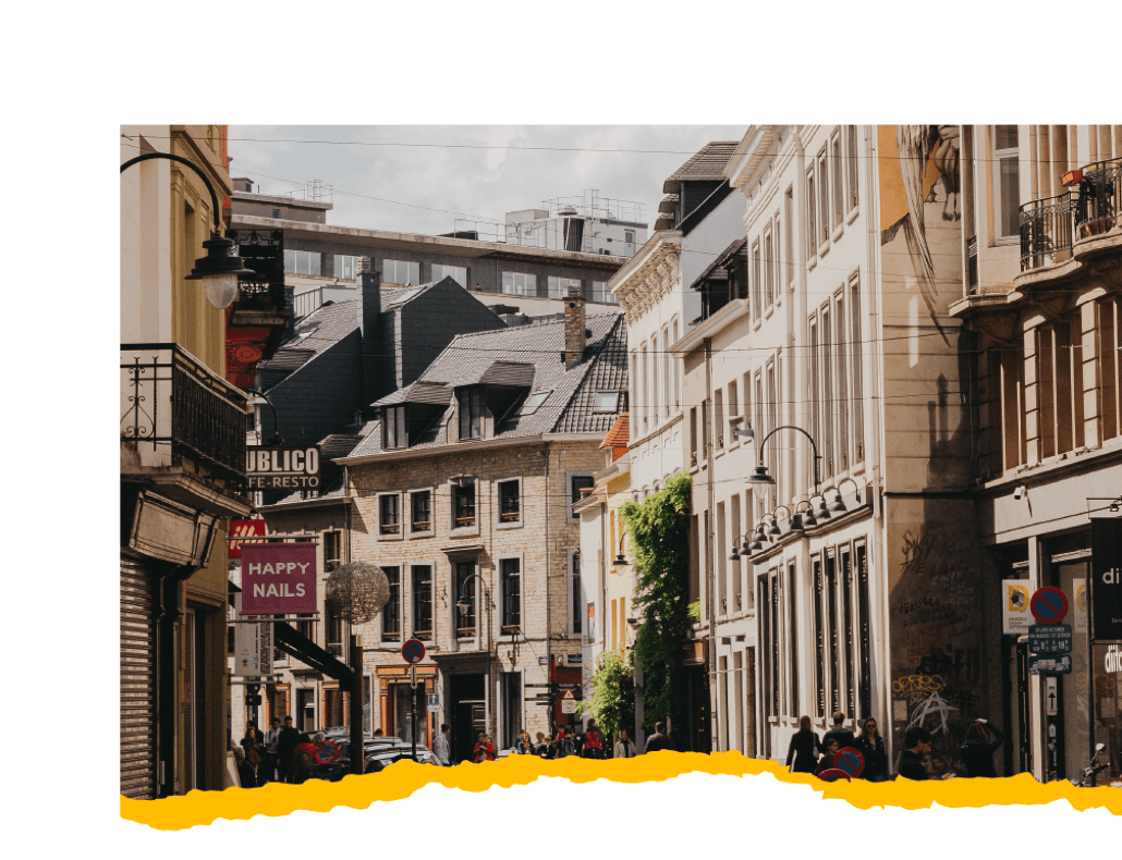 A bustling city street with tall buildings & people strolling along the sidewalks.