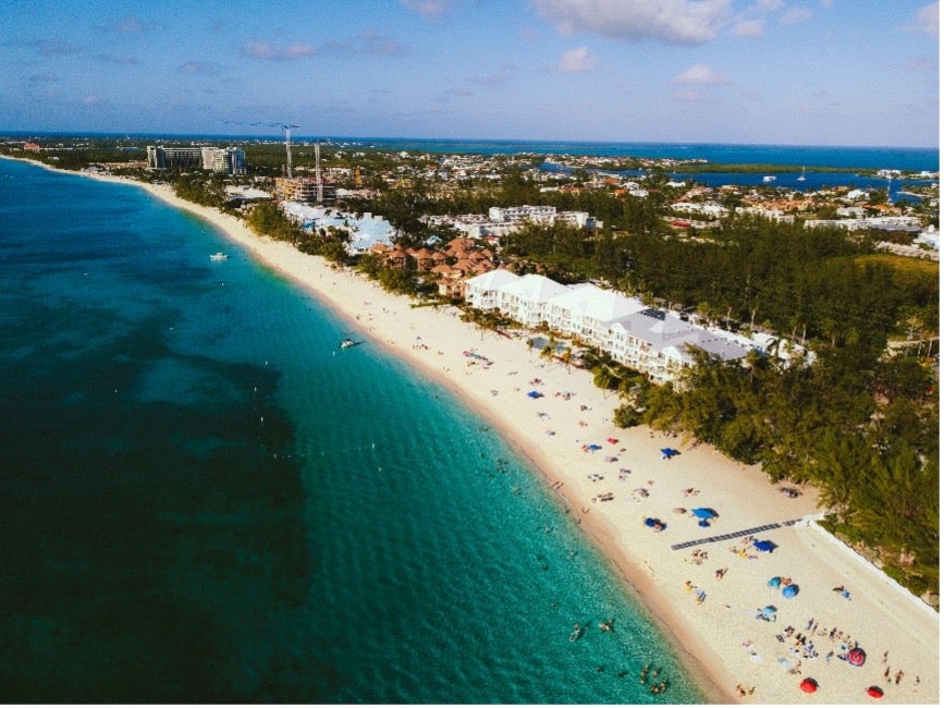 An aerial shot of Cayman Islands features deep blue water and light-colored sand
