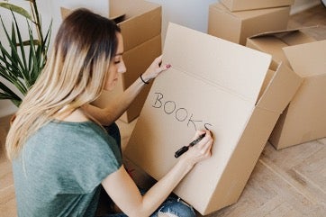 Woman writing on cardboard moving box.