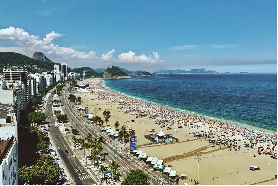 A sunny beach stretches along the curving coastline in Rio de Janeiro, Brazil. 