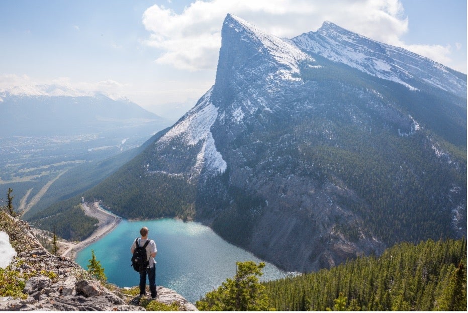 Man stands on a rock overlooking a large lake and a big mountain after his individual move to Canada.