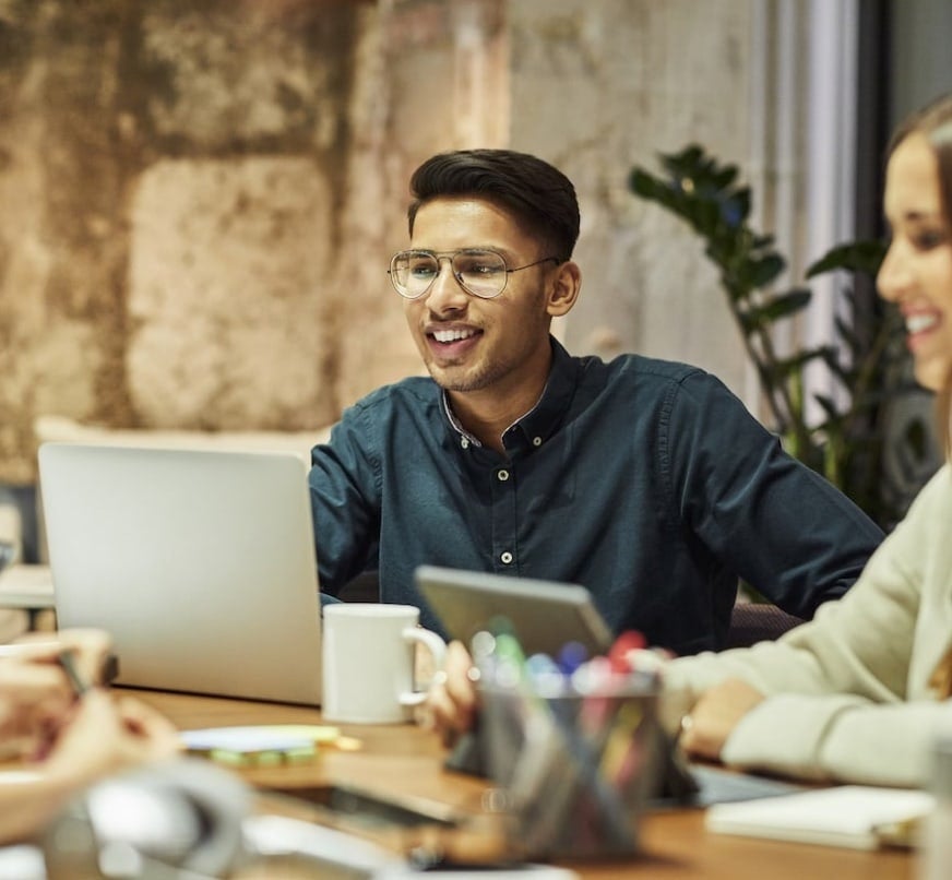 A group of people sitting around a table with laptops & office supplies. A group of people sitting around a table with laptops & office supplies.