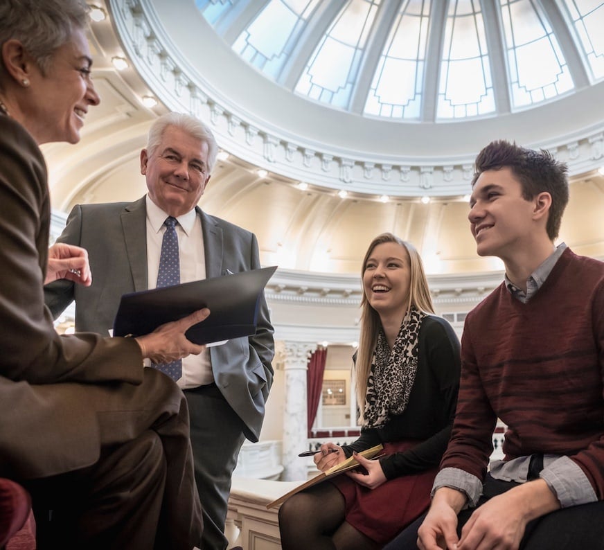 Four people in a big lobby hall & conversing with enthusiasm.