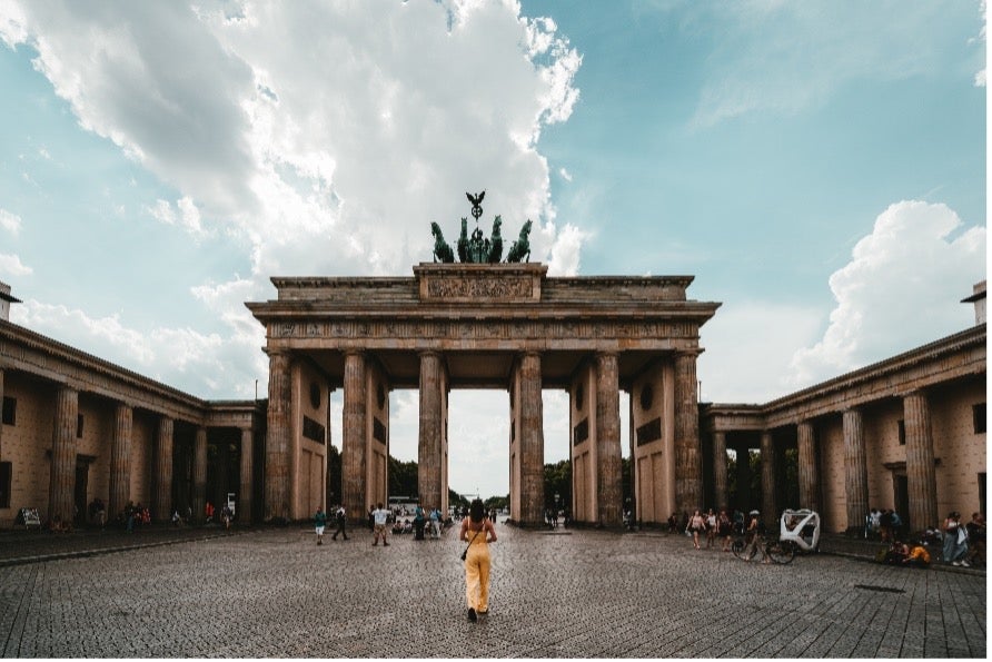 Woman in tan jumpsuit stands in front of the Brandenburg Gate in Berlin, Germany after international relocation.