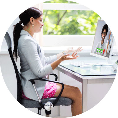 Woman working from home and smiling at her colleague on her laptop with a gray blazer and pink shorts.?fm=webp&q=65