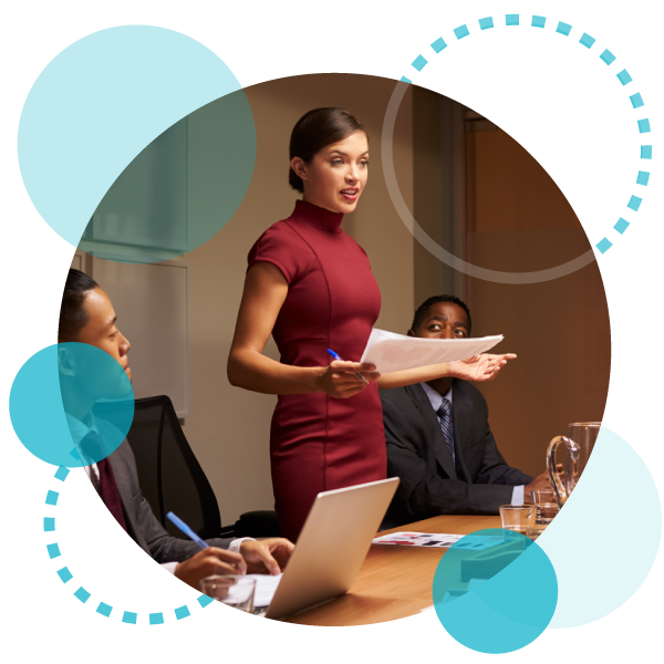 Femme leader confiante debout dans une salle de conférence tenant des papiers et un stylo, entourée de deux de ses collègues qui sont assis ?fm=webp&q=65