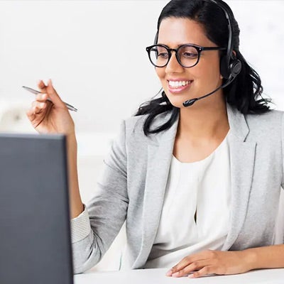 professional woman with a pen in hand and a headset on, looking at her computer to show that a blog on virtual facilitation was one of our most-read leadership articles of 2020