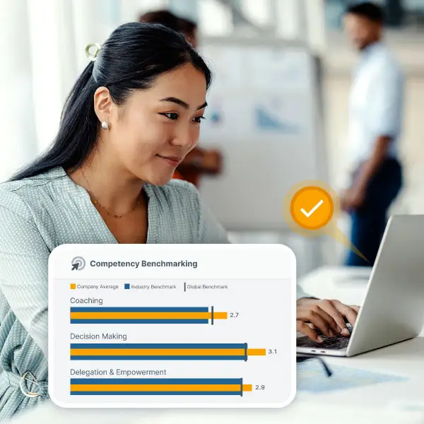woman smiles while working on her laptop. a bar chart layered on top shows that she's looking at company-wide leadership simulation results for skills like coaching, decision-making, and delegation and empowerment compared to industry and global benchmarks