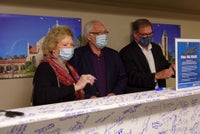Team members pose in front of beam signing event.