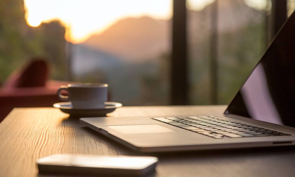 Computer and coffee mug and telephone large windows and sun rising, focus on laptop touch pad.jpg