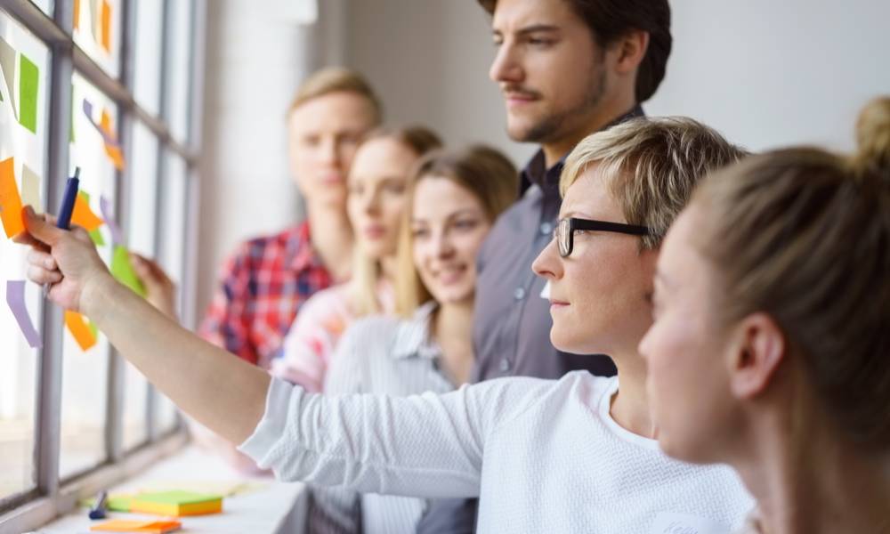 A team of focused work colleagues discussing ideas and brain storming with sticky notes on an office window.jpg