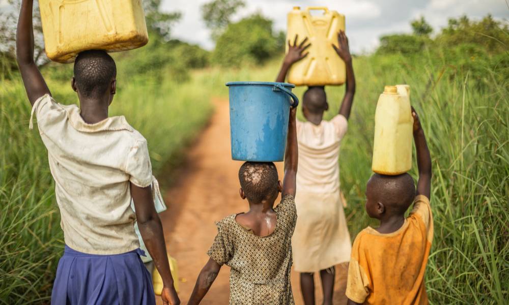 Group of young African children walking with buckets and jerrycans on their head as they prepare to bring clean water back to their village.jpg