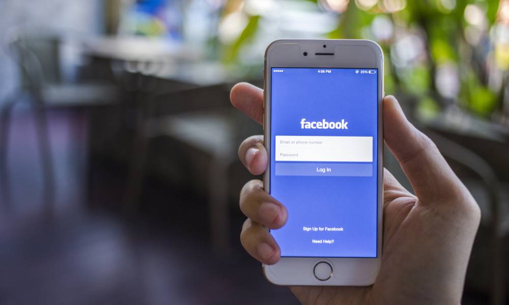 Woman holds phone showing Facebook log in (1).jpg