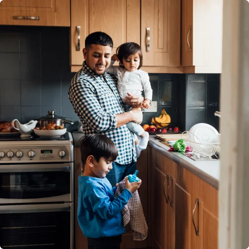 Father carrying his daughter while his son dries some dishes.