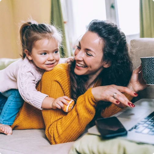 Mother and daughter smile at each other with a laptop in front of them.