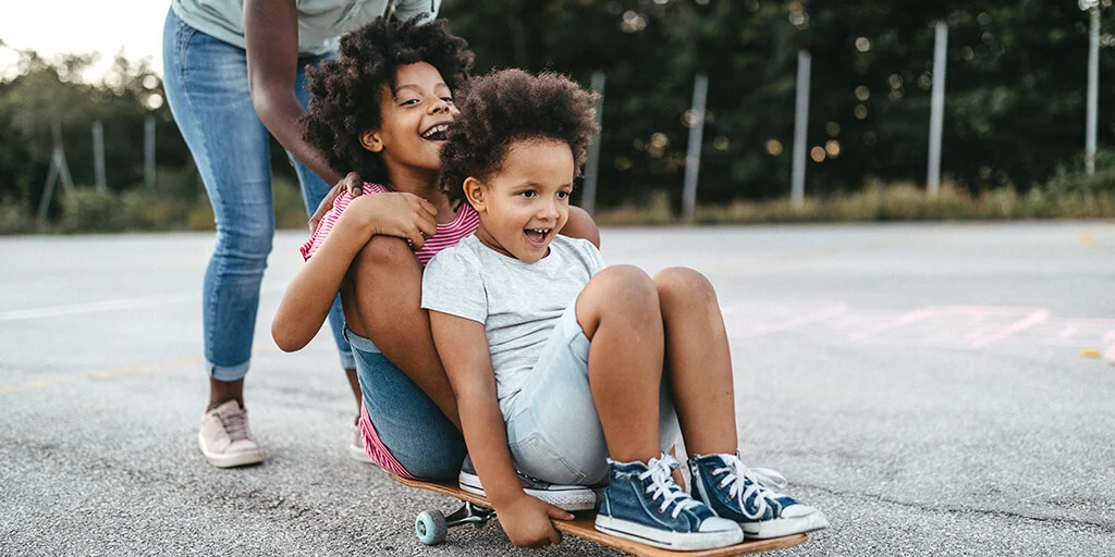 2 kids being pushed on a skateboard.