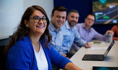 three men and a woman smiling at the camera sat at a meeting desk next to each other