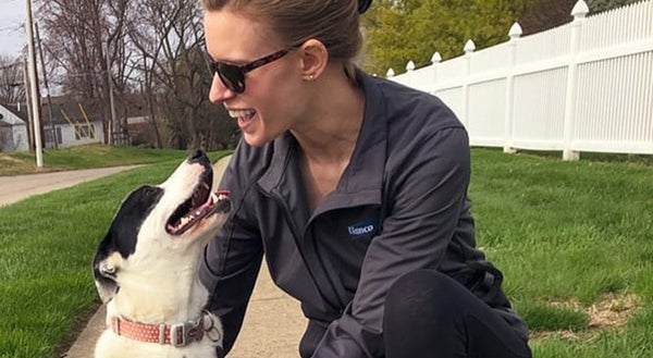woman and dog both looking at each other smiling on a sidewalk