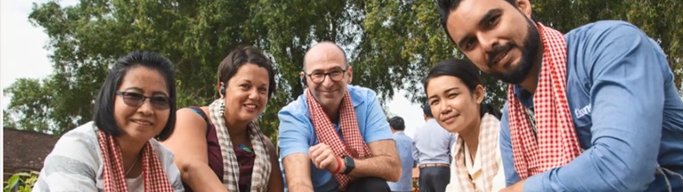 group of five knelt down smiling at the camera whilst touching a plant