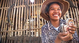 Person vor einem Stall aus Bambus, der ein Huhn hält