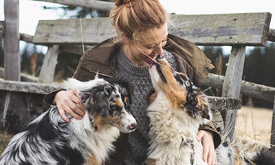 woman sitting down with two dogs smiling at them