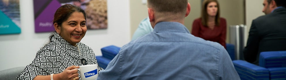 Une femme souriant à un homme assis dans une salle d'attente et tenant une tasse Elanco.