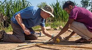 two males knelt down making something out of bamboo