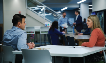 Zwei Frauen und ein Mann lächelnd vor einem Willkommensschild in mehreren Sprachen
