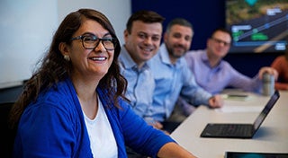 three men and a woman smiling at the camera sat at a desk