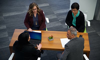 an over head view of three women and a male discussing at a desk