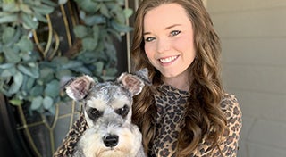 young woman smiling at the camera whilst holding her dog