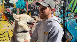 young man looking at his dog and smiling infront of a graffiti wall