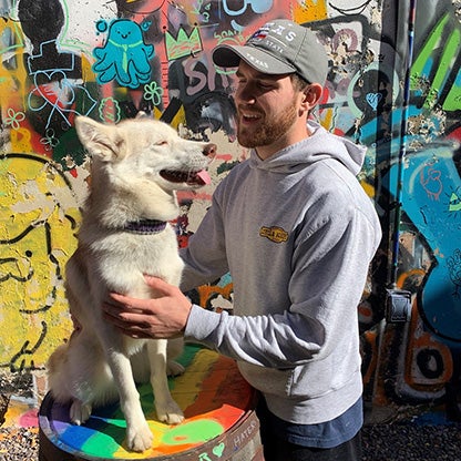a young man looking and stroking his dog in front of a graffiti wall

