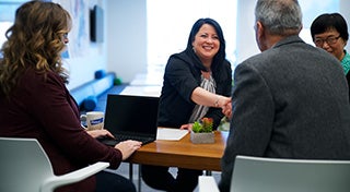 employees at a table having a conversation while 2 shakehands