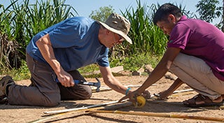 two males knelt down making something out of bamboo