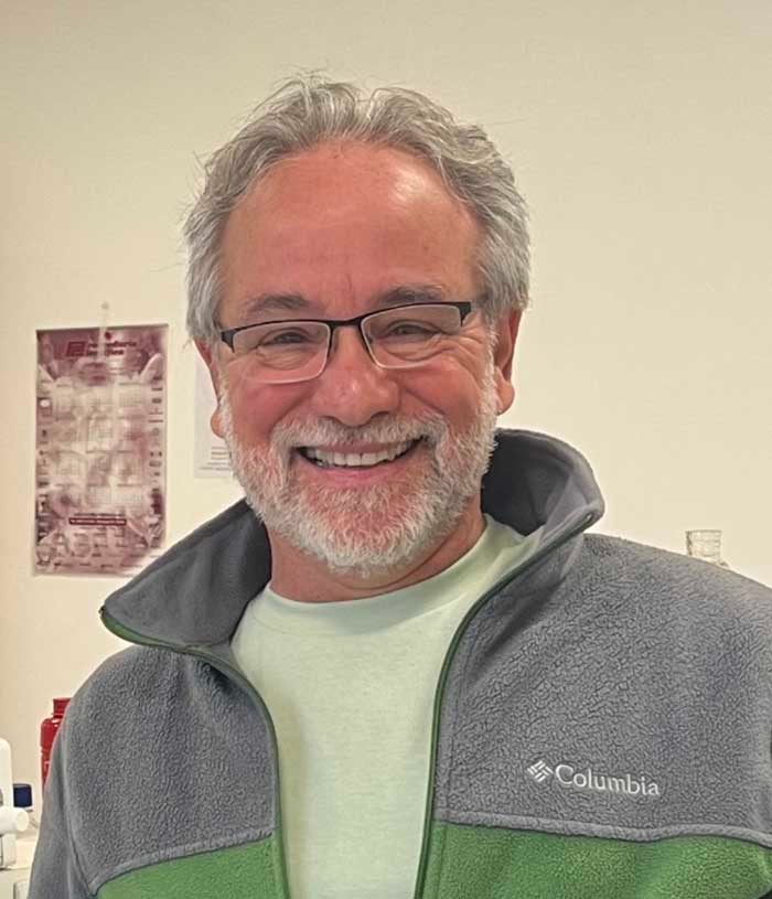 Alberto L. Rosa, a man with white hair and a beard, wears a gray and green Columbia fleece over a lime green t-shirt.