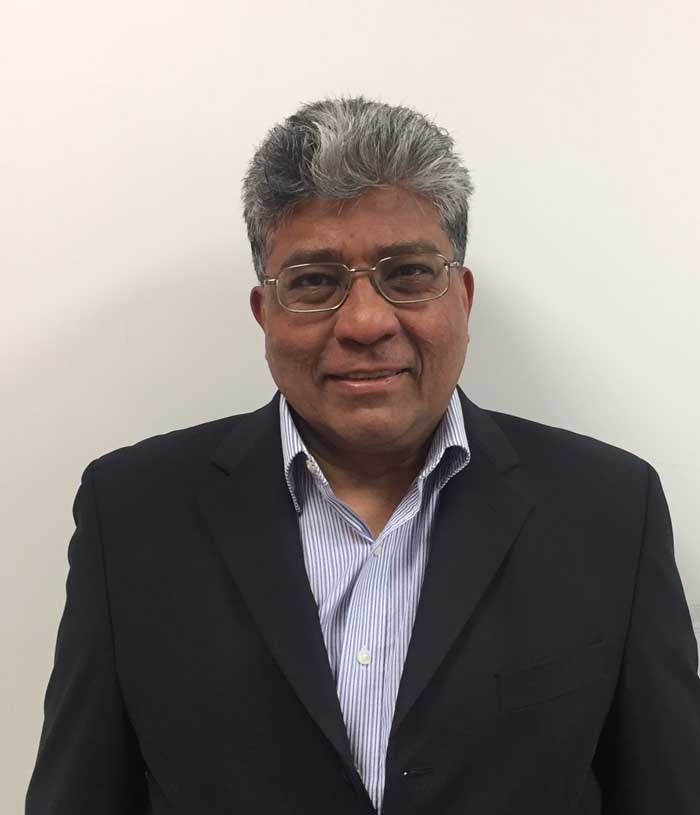 Arne Akbar, a man with short graying hair, in a blazer and striped blue shirt on a tan background.