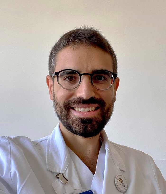 Mauro Monforte, a man with dark hair and a beard wearing round glasses, wears a white lab coat.