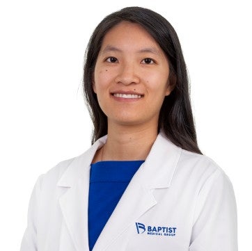Joanne Shung is pictured in her white physician's coat. She is wearing a blue shirt and has long dark hair.