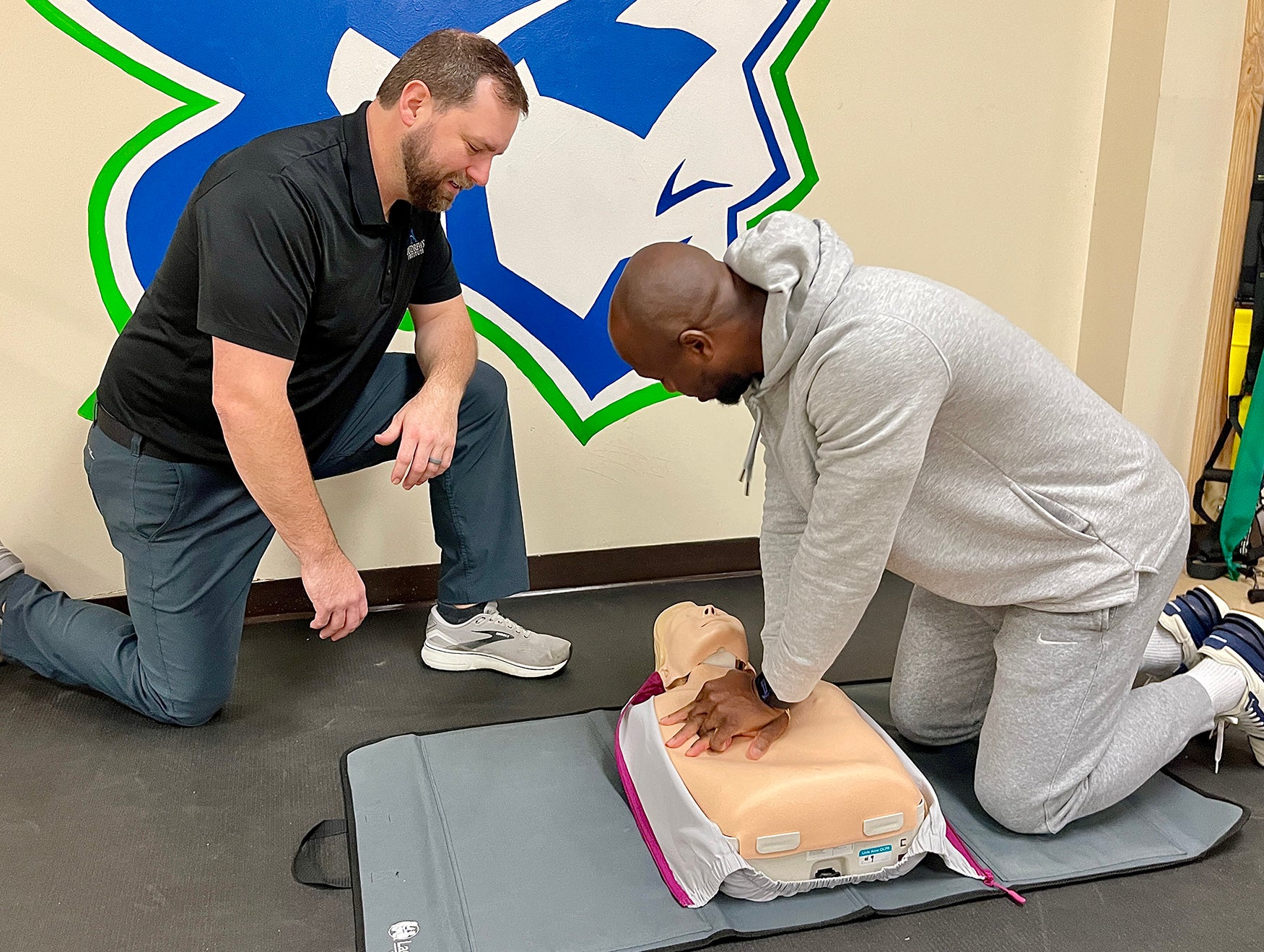 Instructor teaching student CPR on CPR mannequin.