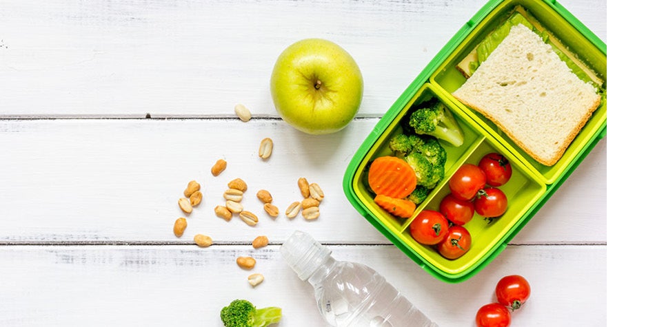 Lunch box with sandwich and vegetables on white table.