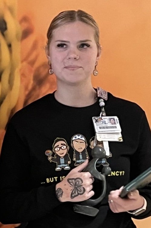 Summerlin Morris, R.N. pictured with her Daisy award for nursing excellence. She has her hair pulled back and is wearing a black shirt. 