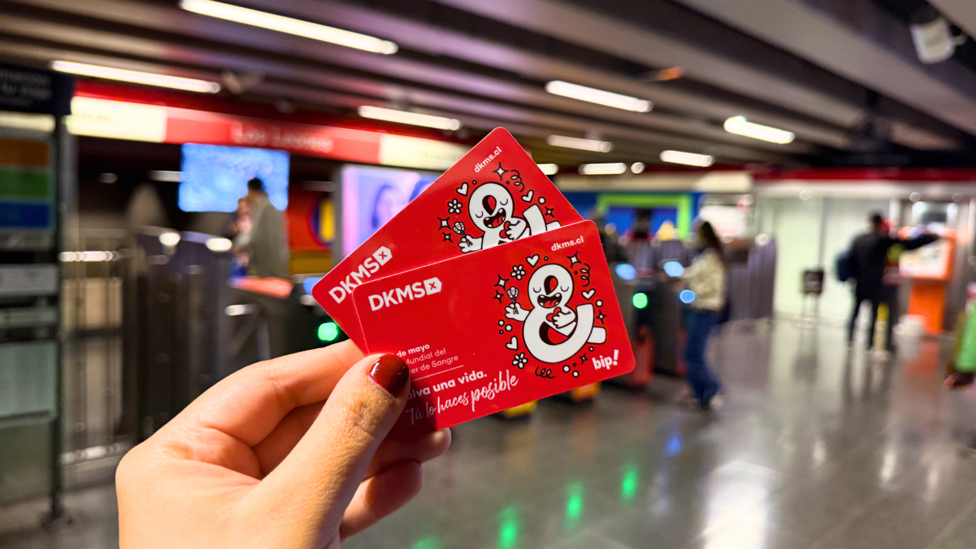 Mano sosteniendo dos tarjetas Bip conmemorativas de DKMS en una estación de Metro de Santiago