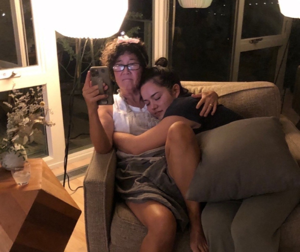 Mama G and Emi Grannis are both sitting in a chair at night with the light on. Emi is curled up in Mama G's lap on her right side. 