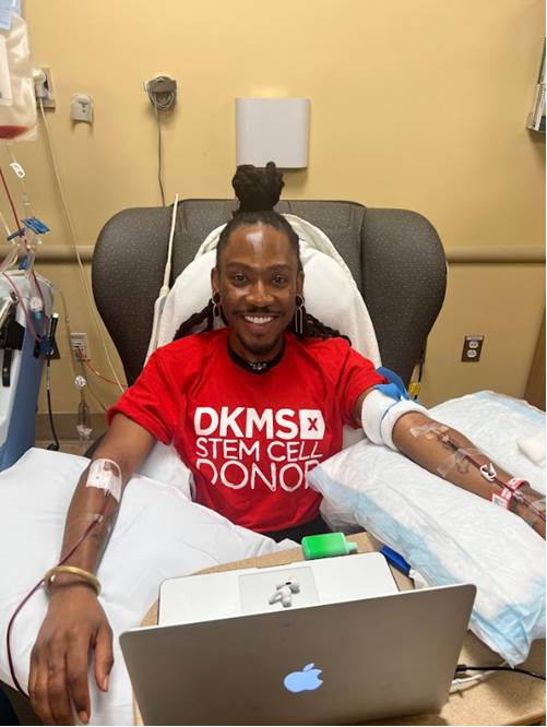 DKMS Blood Stem Cell Donor, Deonte, sitting in a chair donating his stem cells while smiling wearing a DKMS donor shirt. 