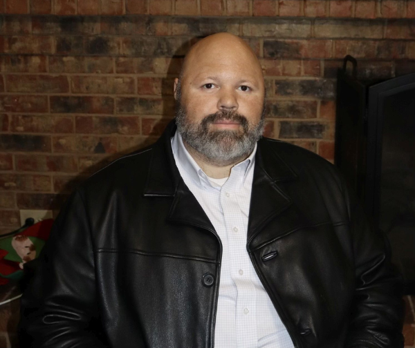 DKMS Patient, Royce, wearing a white shirt and leather jacket while sitting. 