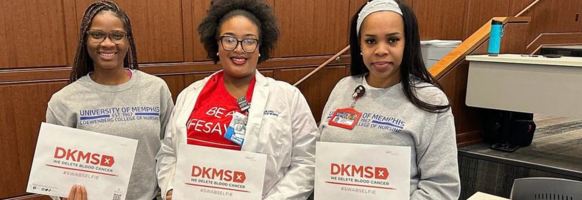 Three nursing students from the University of Memphis smile while holding DKMS registration packets. 