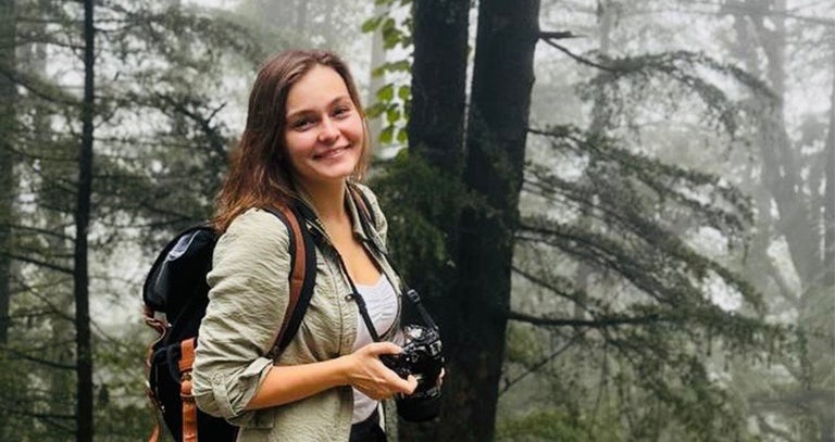 A woman smiling with a camera in the woods