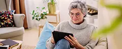 Person sitting on a sofa in a cosy living room, using a tablet with cushions and books nearby.