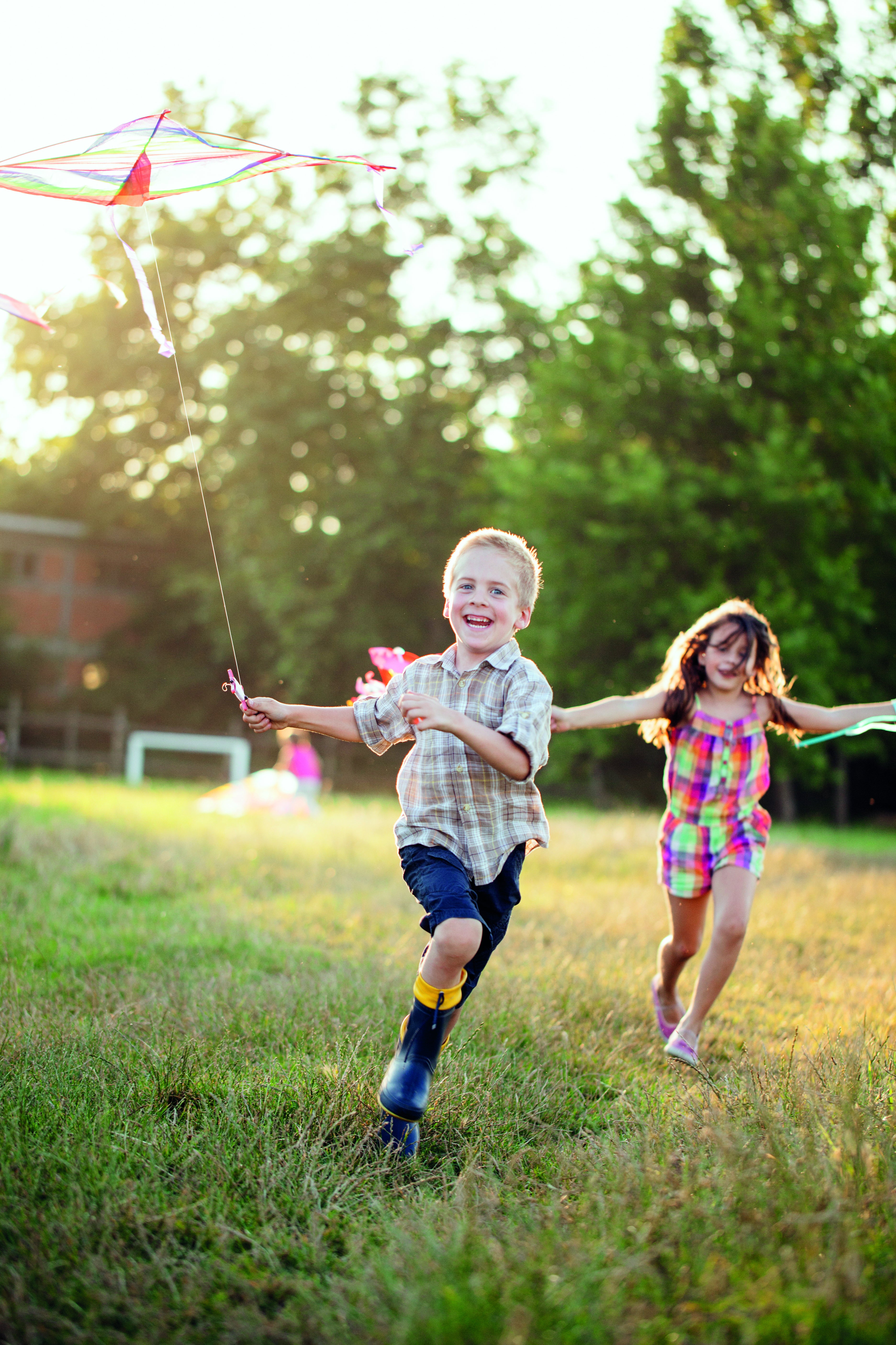 Girl and boy with kite running through a field in the summer